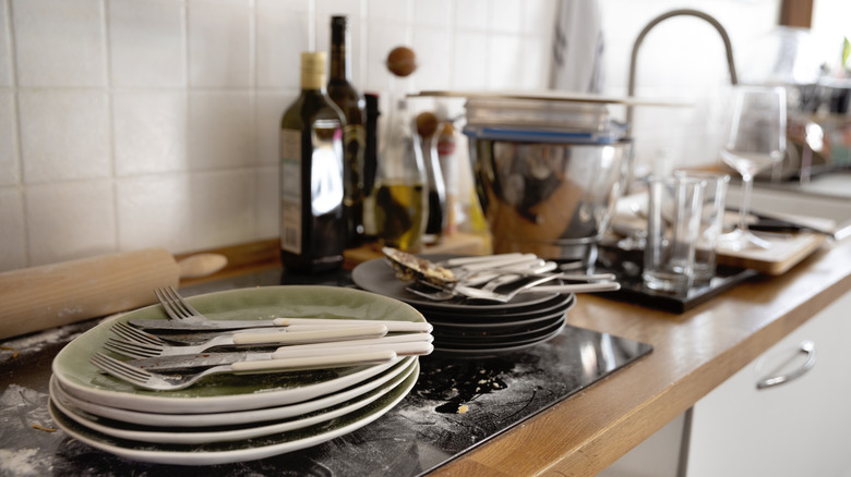 Plates and utensils stacked together on cluttered kitchen countertop