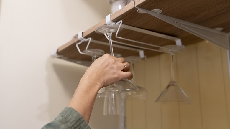 Hand reaching for a glass hanging under a cabinet shelf