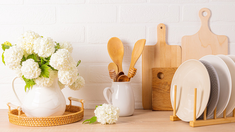Kitchen decor with utensils and pitcher with white flowers against a white brick wall
