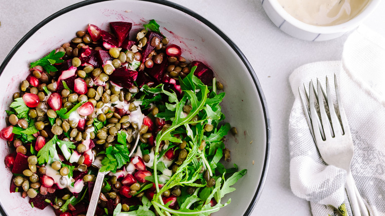 black lentils over a green salad with pomegranate and roasted beets in a white serving bowl