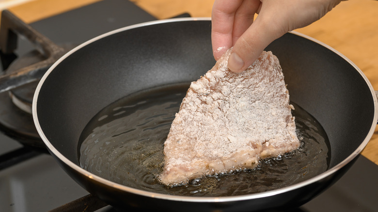 Someone places a dredged pork chop in a pan of oil to fry it