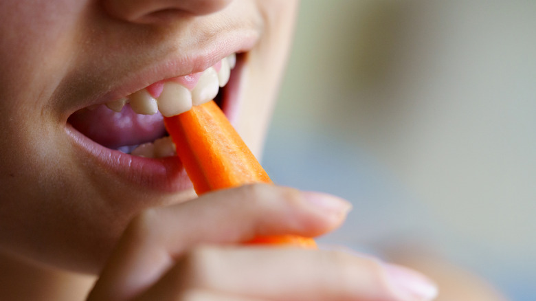 A person biting a raw carrot stick