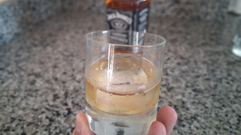 hand holding Jack Daniel's glass on the rocks with the bottle in the background