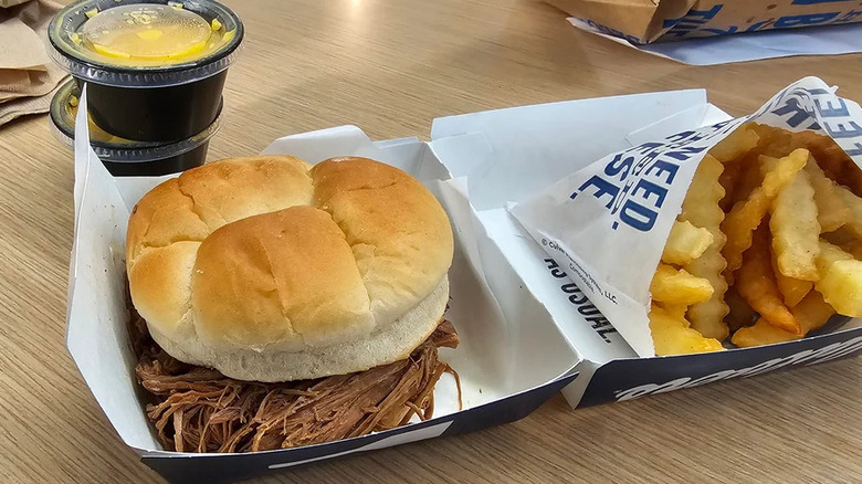 View of Culver's Beef Pot Roast sandwich on a table with cheese sauce and fries