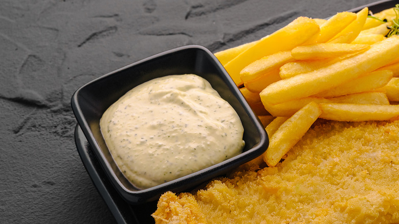 A Fried fish and chips platter sits beside a dish of tartar sauce.