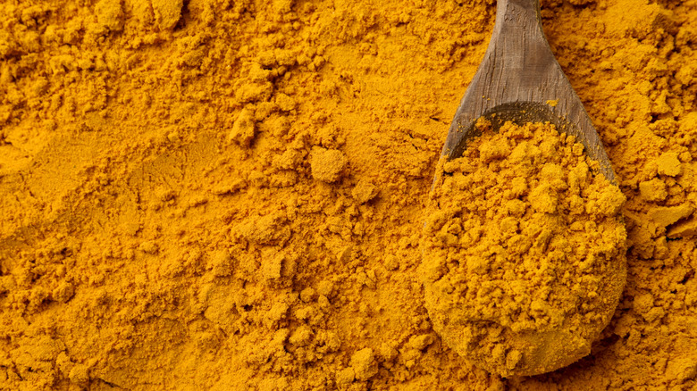 Wooden spoon filled with curry powder laying atop curry powder