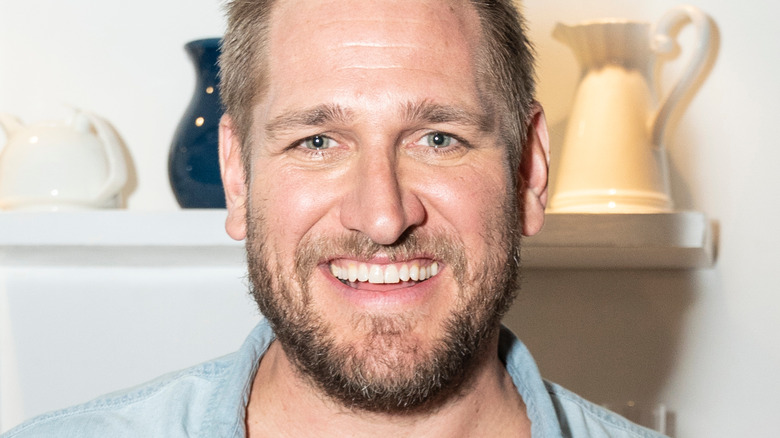 Curtis Stone smiling and holding sandwiches
