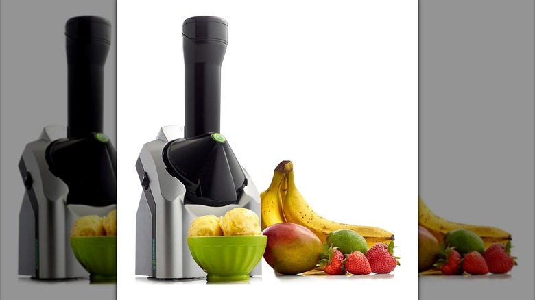 Yonanas Classic Frozen Fruit Soft Serve Maker appliance next to bowl of yellow ice cream and fresh bananas, strawberries, mango, and lime