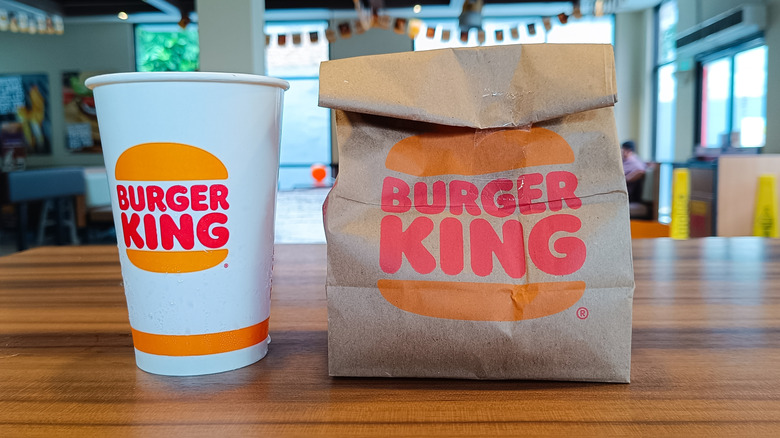 a Burger King bag and cup set side by side on a wooden table inside the restaurant