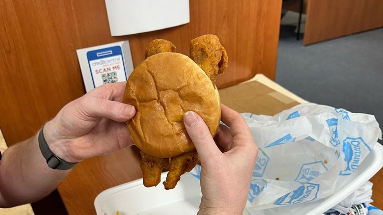 Hands holding Captain D's Giant Fish Sandwich over desk