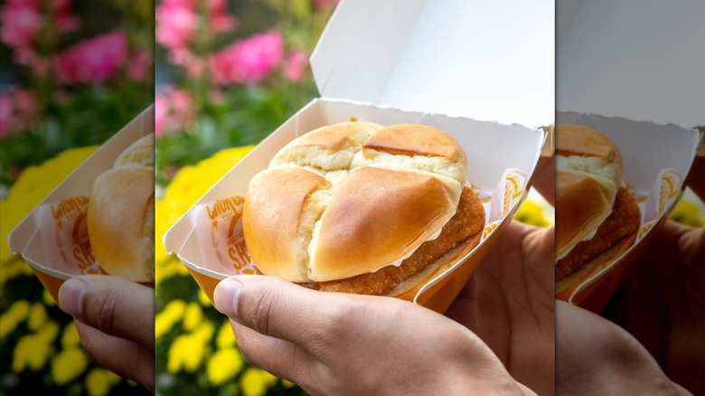 Hand holding Church's Texas Chicken's Fish Sandwich in paper container