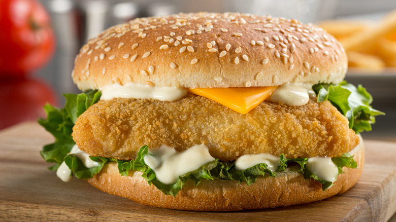 Fish sandwich with lettuce, cheese, and tartar sauce on wooden board