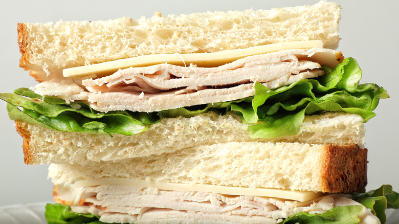 A sandwich with cheese, turkey, and lettuce on white bread sits on a plate.