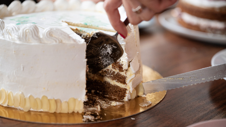 Person slicing a piece of cake on a board