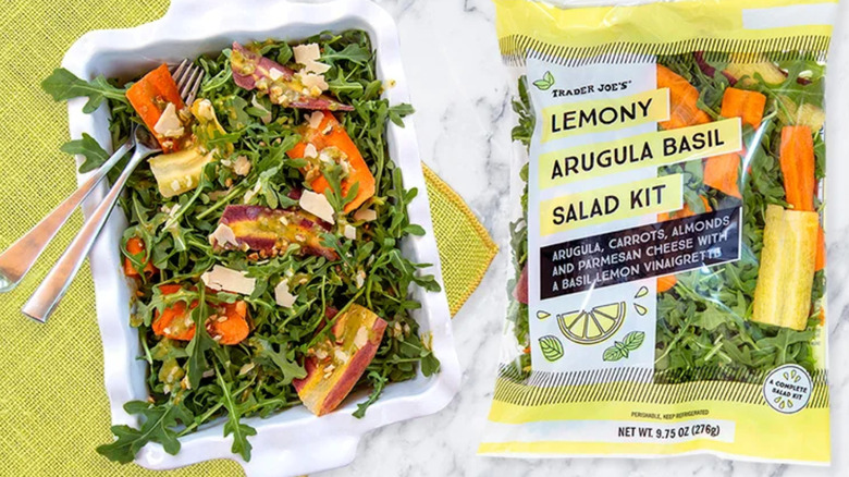 A Trader Joe's Lemony Arugula Basil Salad Kit on a table next to a bag of the same product