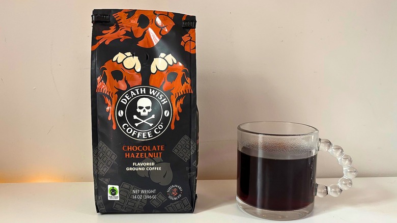 Bag of Death Wish Chocolate Hazelnut coffee next to a clear mug of black coffee on a white table