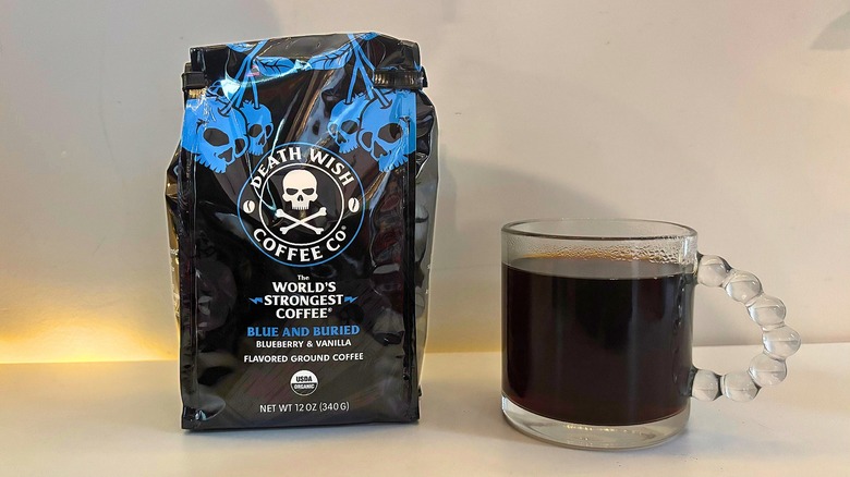 Bag of Death Wish Blue and Buried coffee next to a clear mug of black coffee on a white table