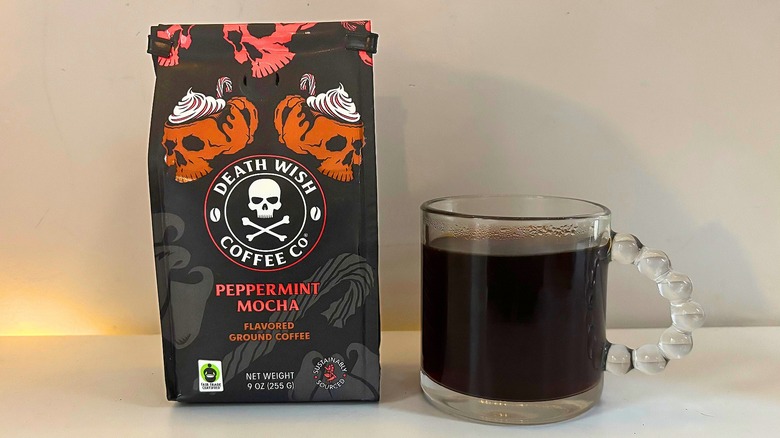 Bag of Death Wish Peppermint Mocha coffee next to a clear mug of black coffee on a white table