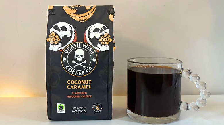 Bag of Death Wish Coconut Caramel coffee next to a clear mug of black coffee on a white table