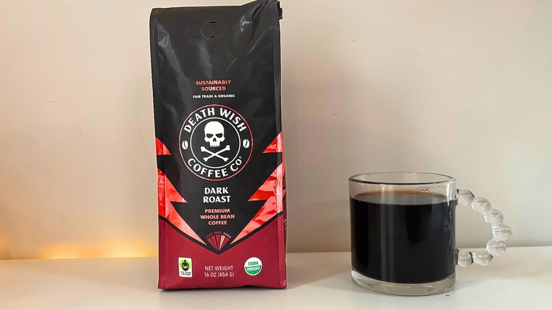 Bag of Death Wish Dark Roast coffee next to a clear mug of black coffee on a white table