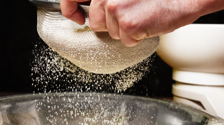 Sifting flour through fine mesh sieve