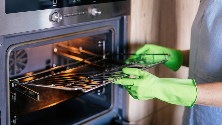person cleaning oven with rubber gloves