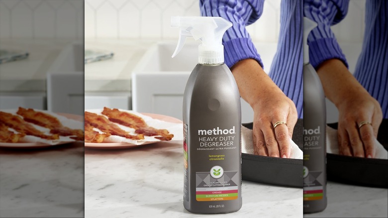 A gray bottle of Method Heavy Duty Degreaser cleaning spray on a kitchen counter next to a plate of bacon