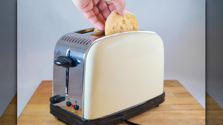A person putting an english muffin into a toaster