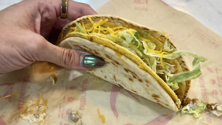 Hand holding Taco Bell Cheesy Gordita Crunch on wrapper.