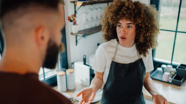 Young woman wearing apron arguing with customer