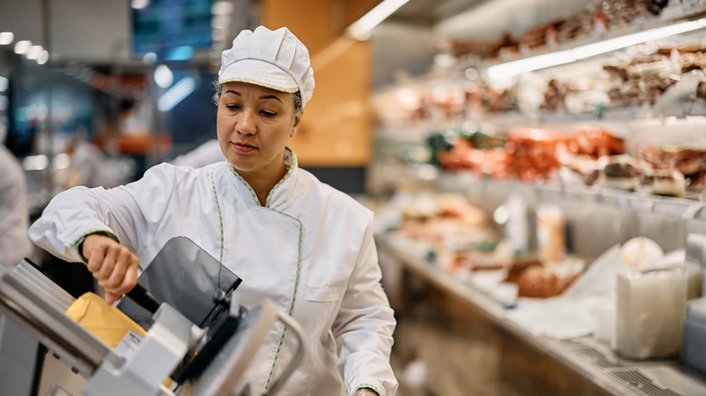 Supermarket clerk using slicer while working at delicatessen section