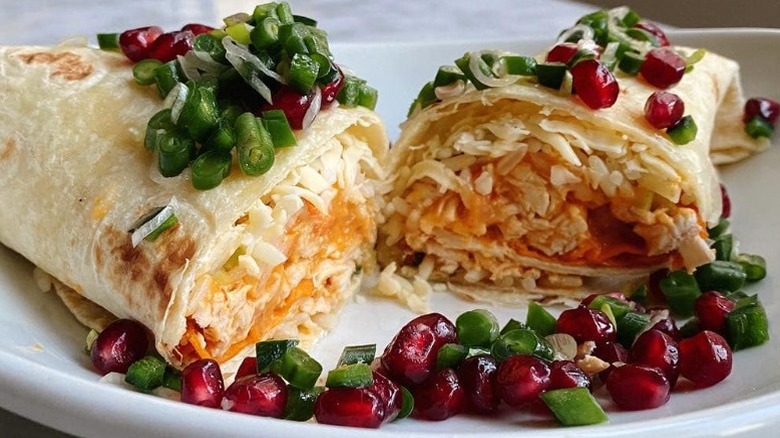burrito filled with rice and topped with greens and pomegranetes