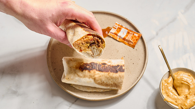 hand picking up burrito from the plate