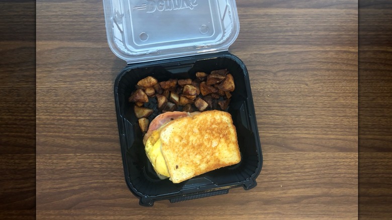 Denny's Moons Over My Hammy breakfast sandwich with potatoes in takeout container