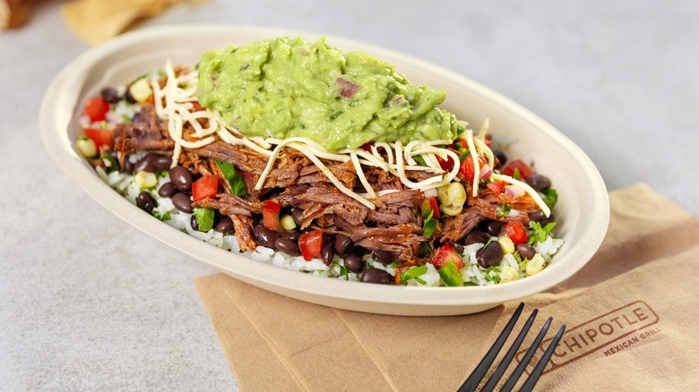 Chipotle burrito bowl on a grey table with napkins and a plastic fork
