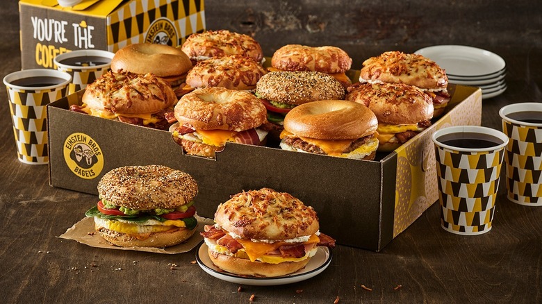 Box full of Einstein Bros. Bagel sandwiches with cups of coffee and plates beside it