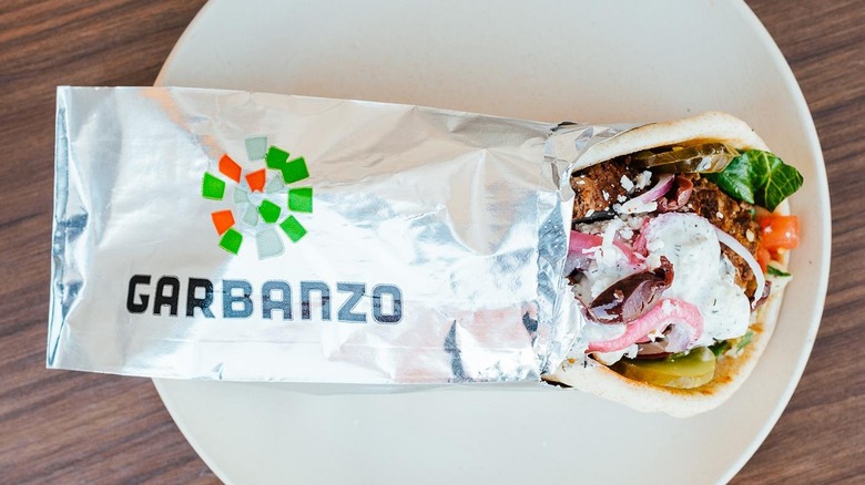 Wrapped Garbanzo pita sandwich sitting on a plate on a wooden table