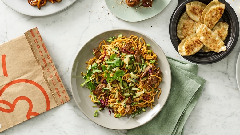 Several Noodles & Company dishes with a branded paper bag beside them