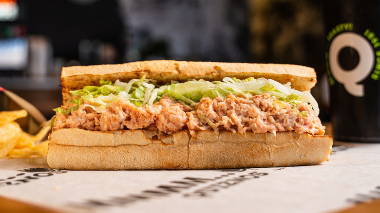 Toasted Quiznos sub on branded paper with chips and a drink beside it