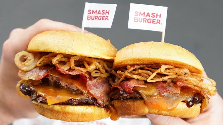 Two hands holding smashburgers with little flags