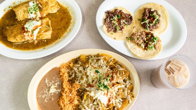 Three platters of food from El Taco Burrito including tamales and nachos smothered in green chile