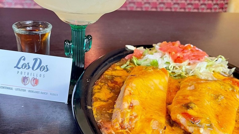 A plate of burritos smothered in green chile sauce sits on a table with a Los Dos Portrillos card to the left.