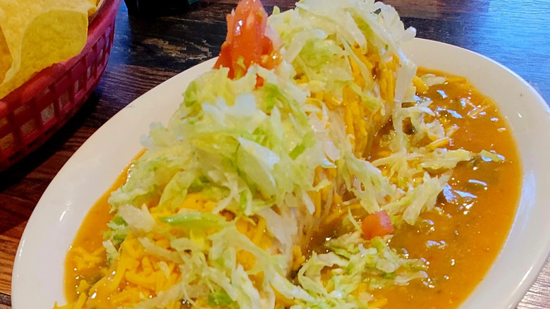 A buritto smothered in green chile sauce and topped with cheese shreds with a Santiago's "faithfully authentic" sign in the background