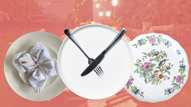 Several white plates with decorative patterns and folded napkins against a red backdrop
