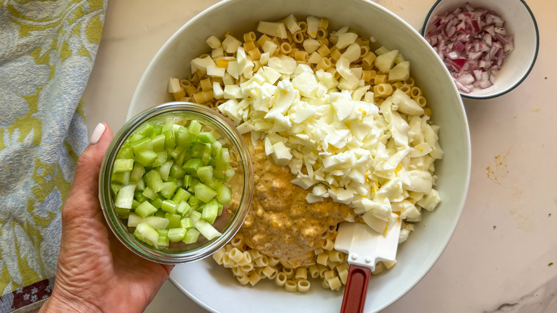 hand adding celery to bowl with pasta salad ingredients