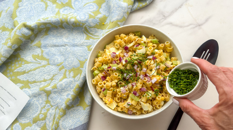 adding chives to serving bowl of deviled egg pasta salad