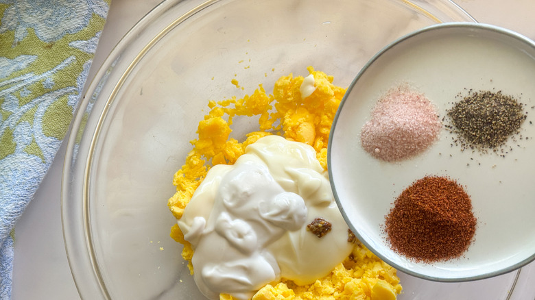 adding spices to bowl with mayo and egg yolks