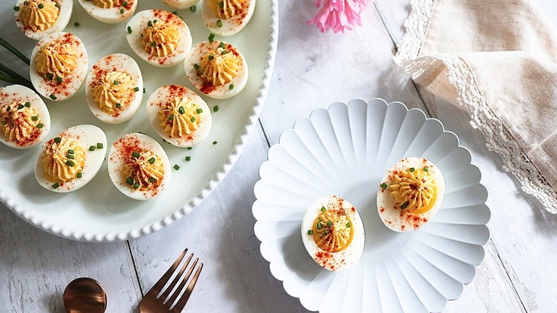 Deviled eggs topped with paprika and served on white plates and a big platter