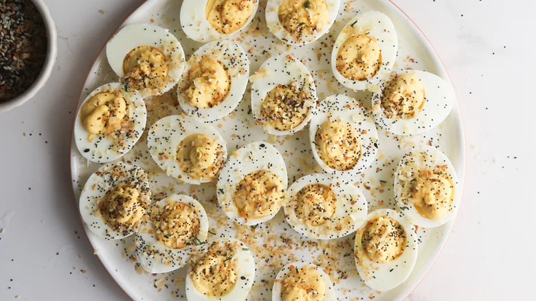 Everything bagel-inspired deviled eggs on white plate sprinkled with everything bagel mix