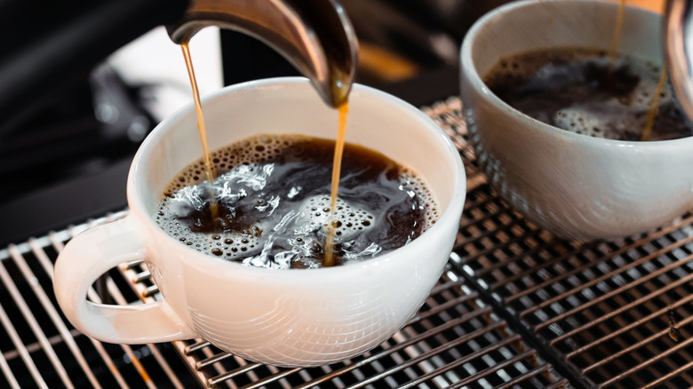 pouring full cup of coffee from espresso machine